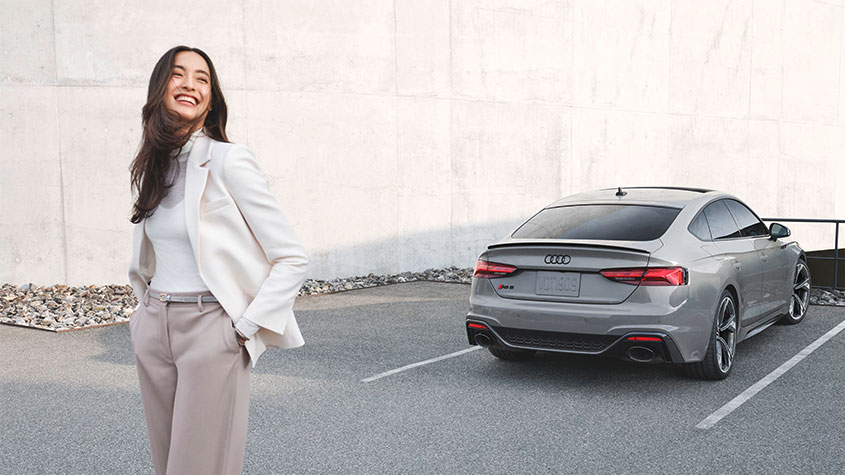 A woman standing in front of a Audi vehicle. 