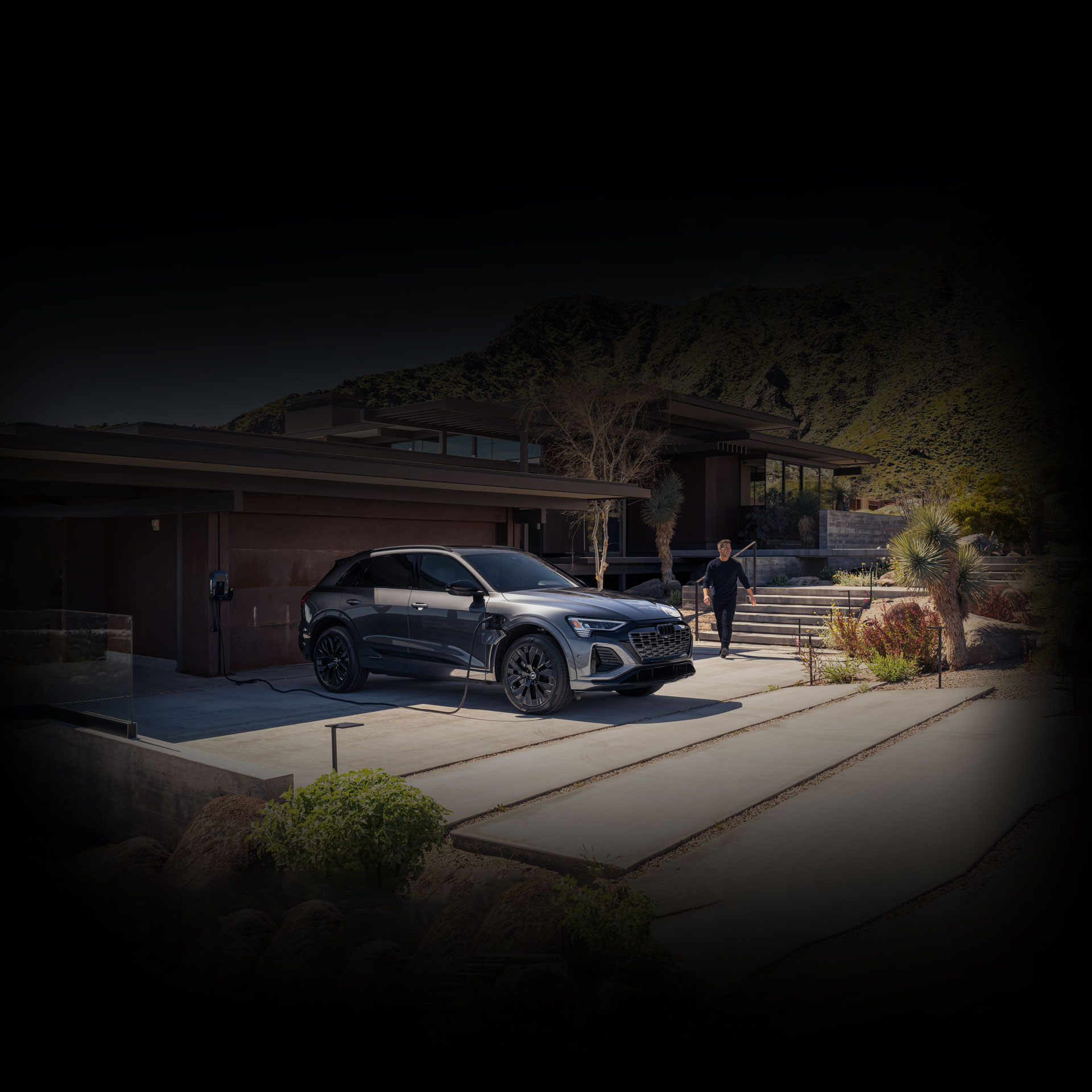 A man approaching his black Audi Q8 e-tron as it charges in front of a modern building. 