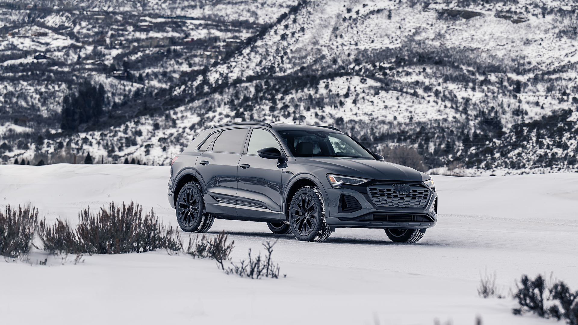 A dark gray Audi Q8 e-tron parked in the snow in a mountainous landscape.