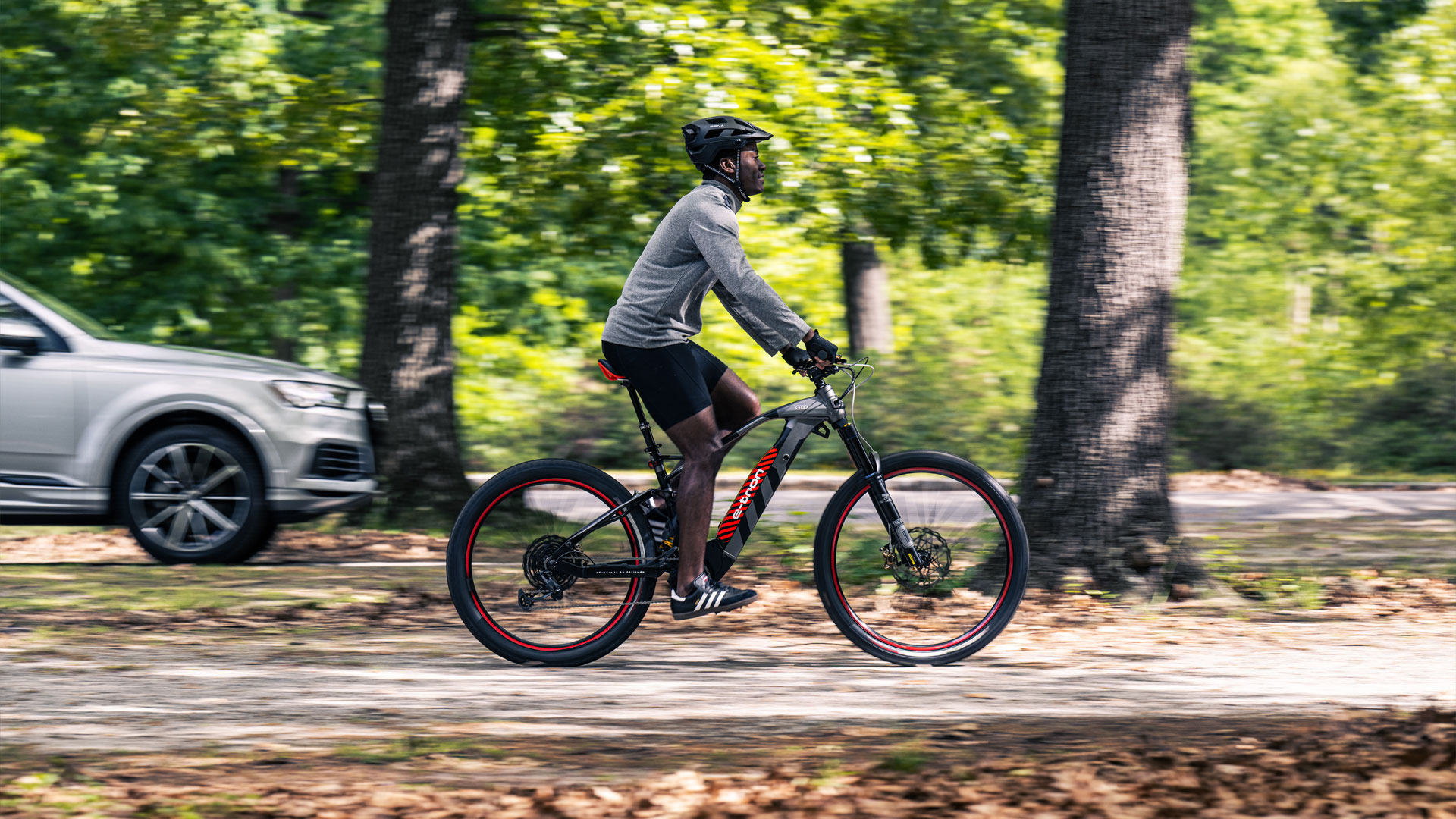 A man riding his Audi electric mountain bike down a tree lined street.