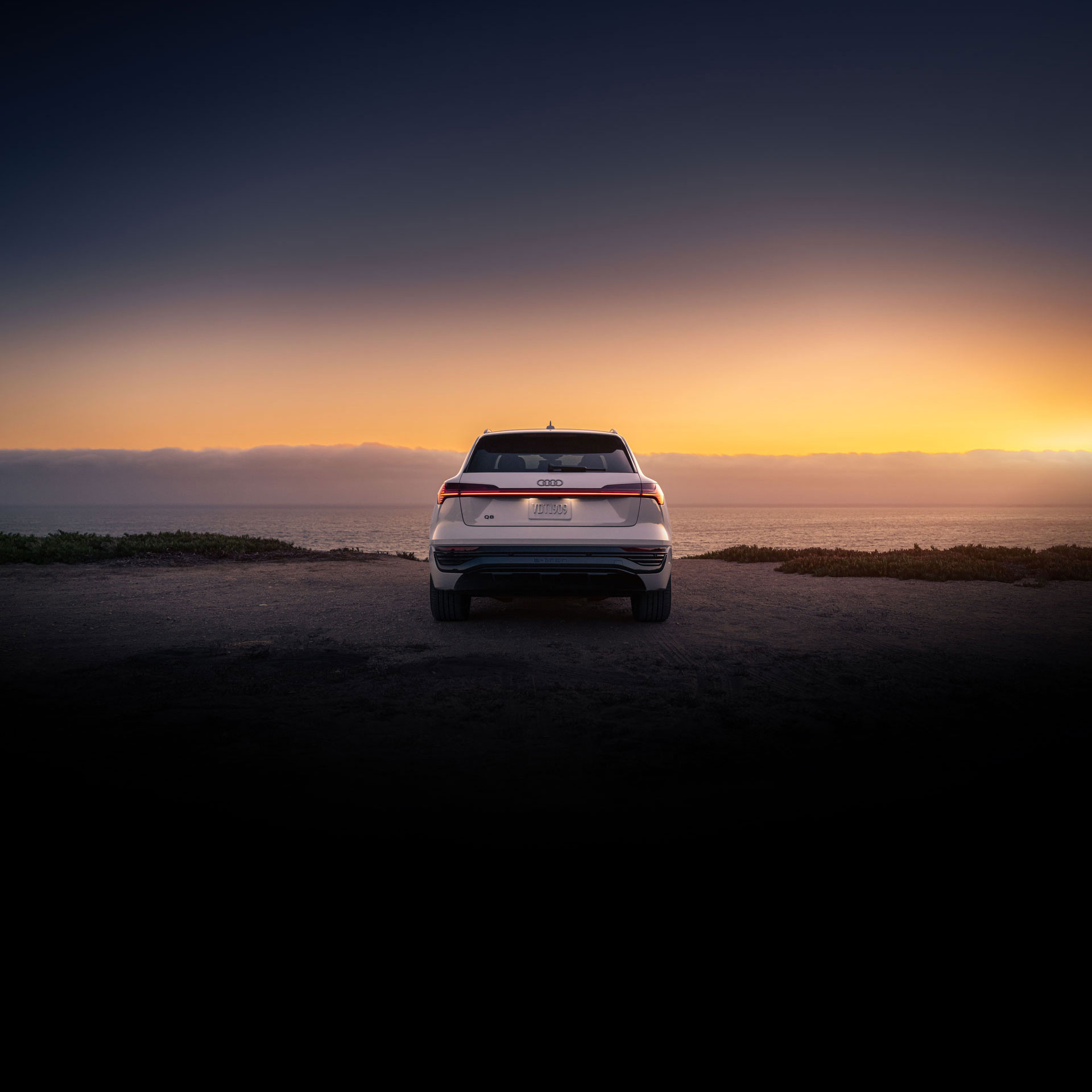 Rear view of a white Audi Q8 parked at the waterfront during sunset. 