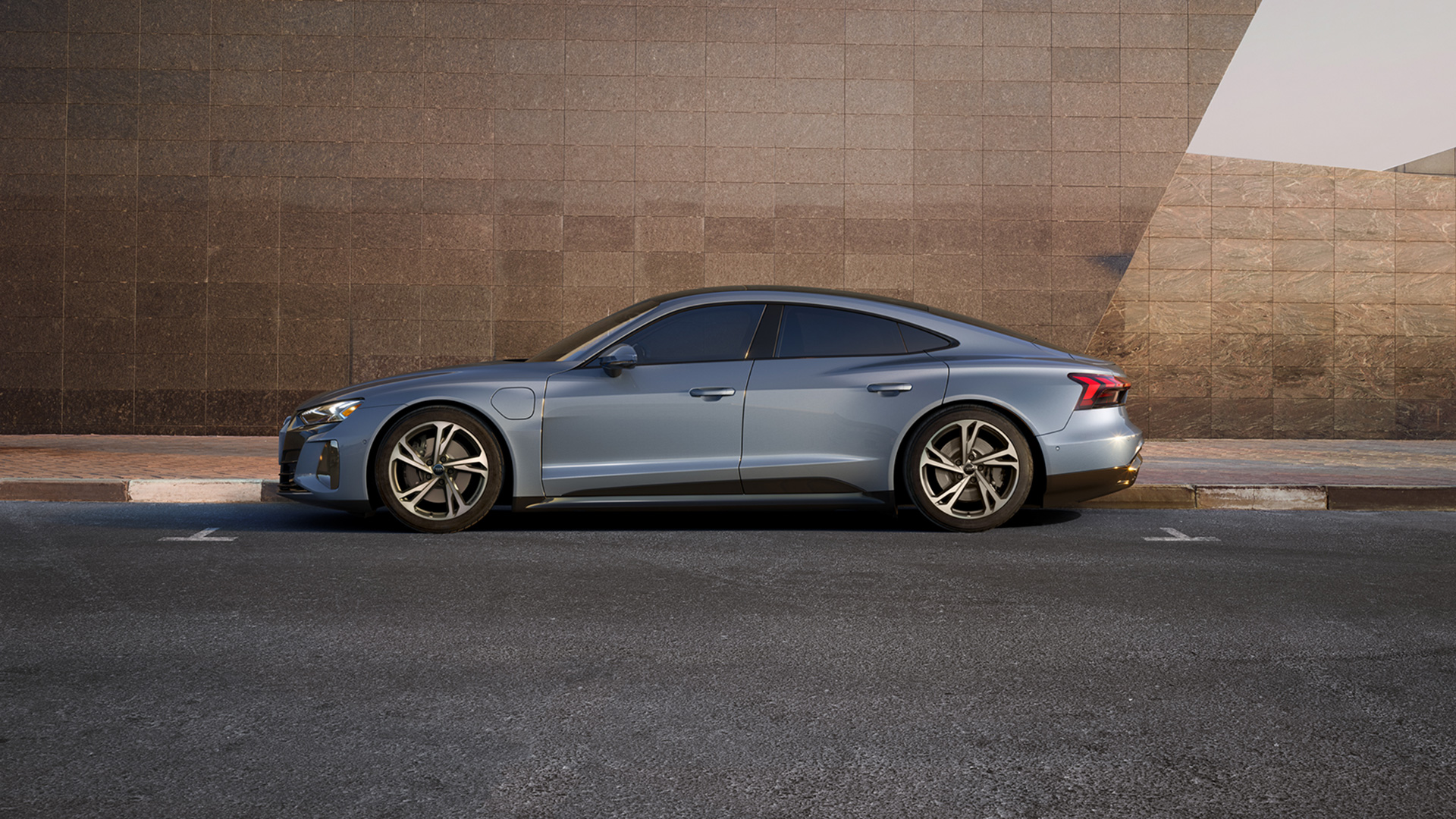 Side profile of an Audi e-tron GT parked in front of a tiled wall. 