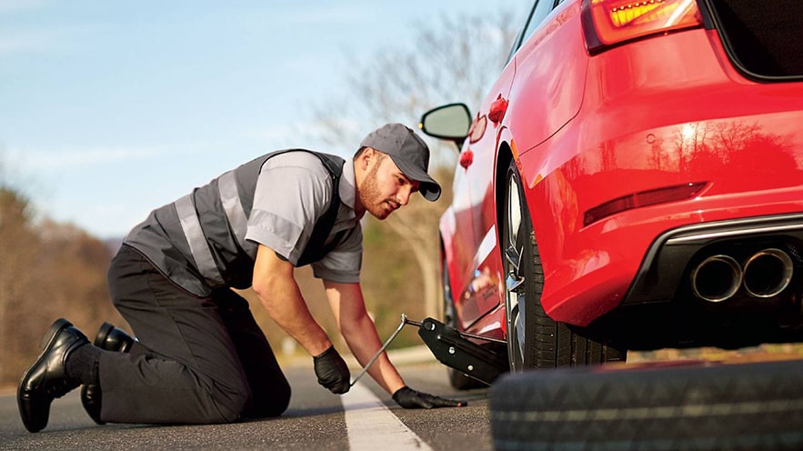 An Audi mechanic working on a car on the side of the road.