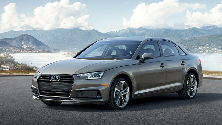 Photo of an Audi A4 parked in the forefront with a pictuesque mountain range and lake in the background. 