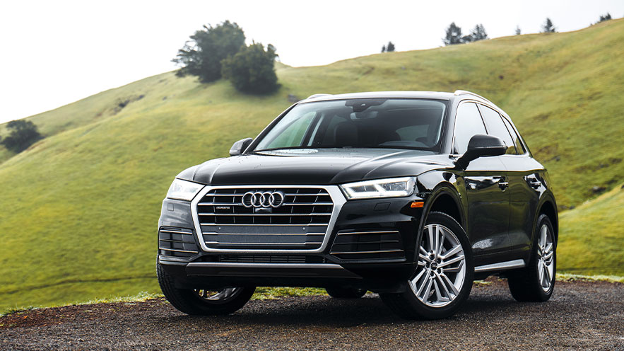 Photo of an Audi Q5 parked near a green hill on a spring day.